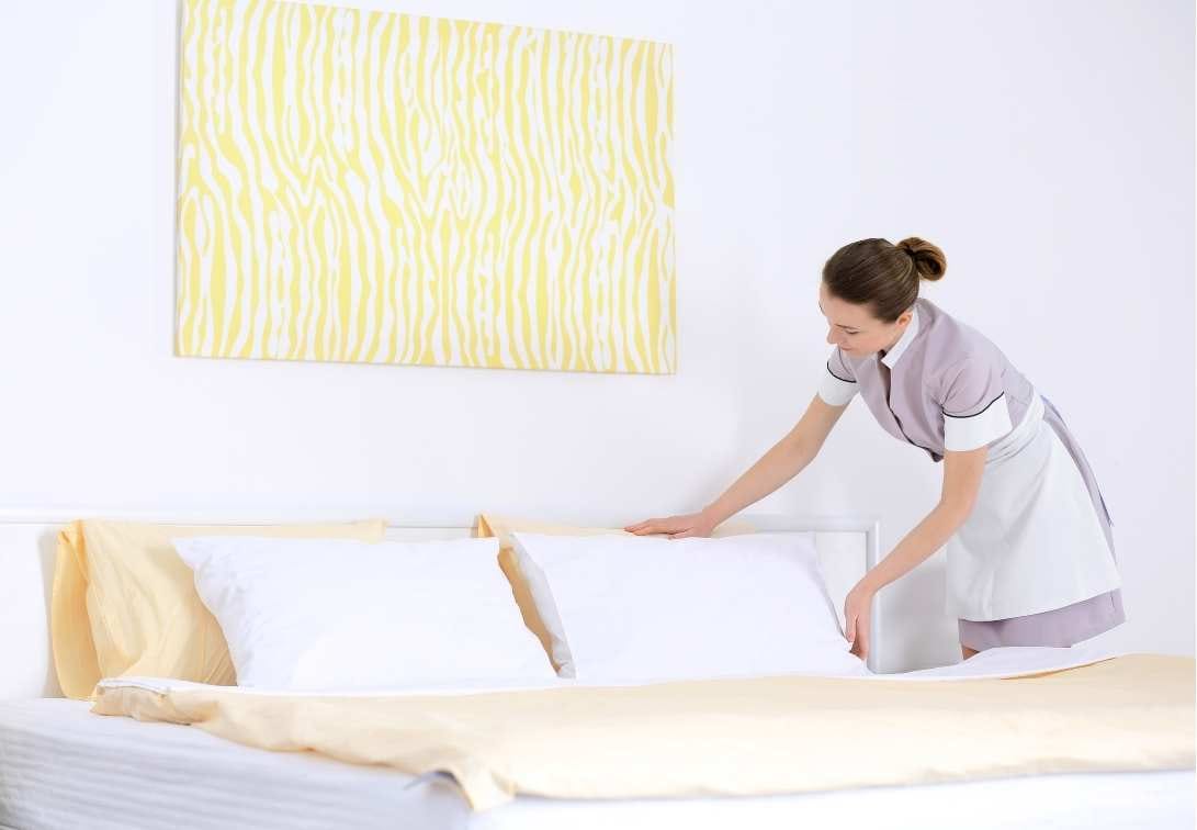 Zimmermädchen legt Handtücher auf ein frisch bezogenes Hotelbett
