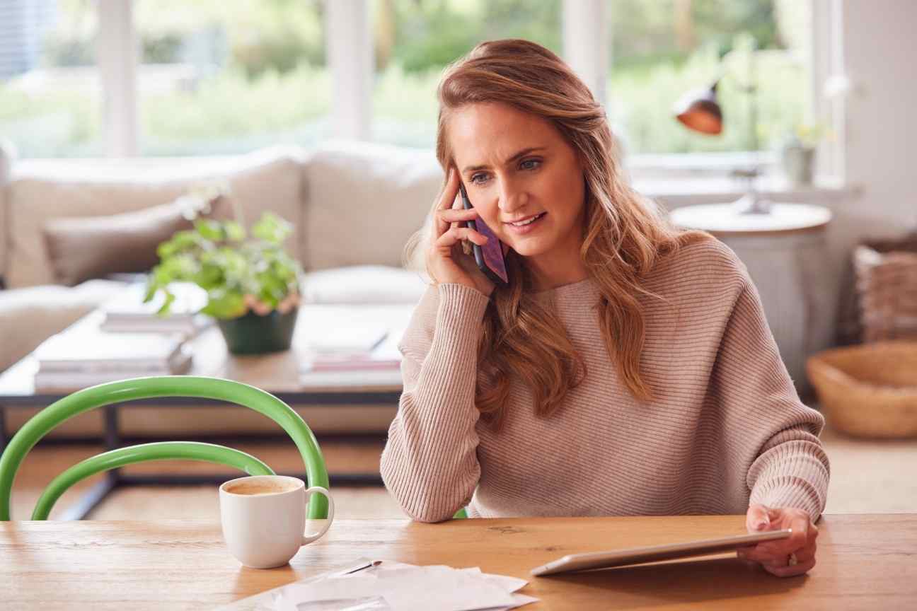 Frau telefoniert am Esstisch und macht sich Notizen